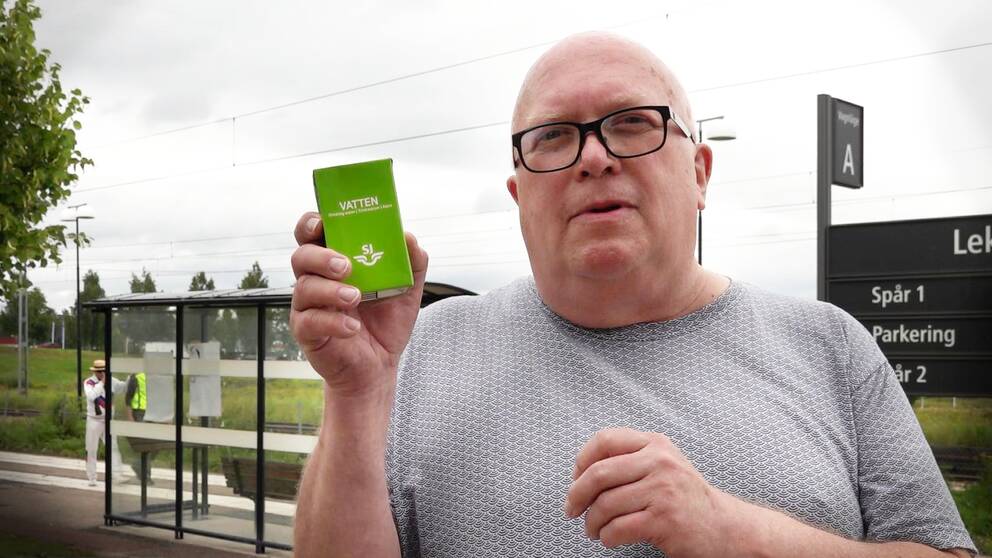 En man med glasögon står vid en järnvägsstation i Leksand. Han håller upp en grön tetraförpackning med vatten som tågföretaget SJ bjöd på när tåget stod till.