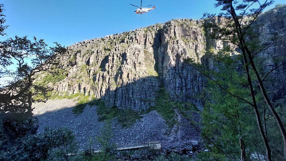 En helikopter vinschar ner en person för att rädda folk som sitter på en bergkant.