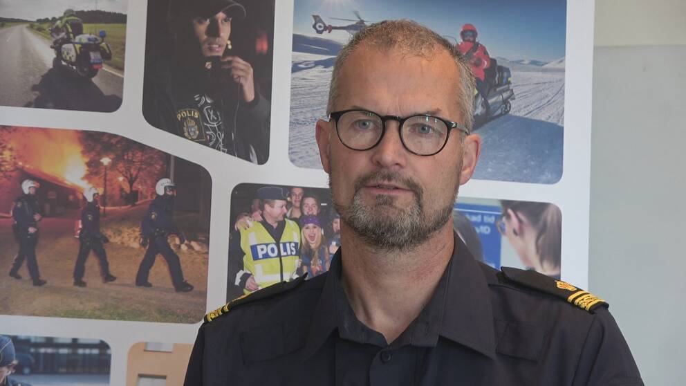 en medelålders man med glasögon, i polisskjorta, framför en vägg med bilder på poliser i arbete