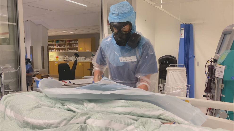 En vårdpersonal i full skyddsutrustning står vid en sjuksäng.