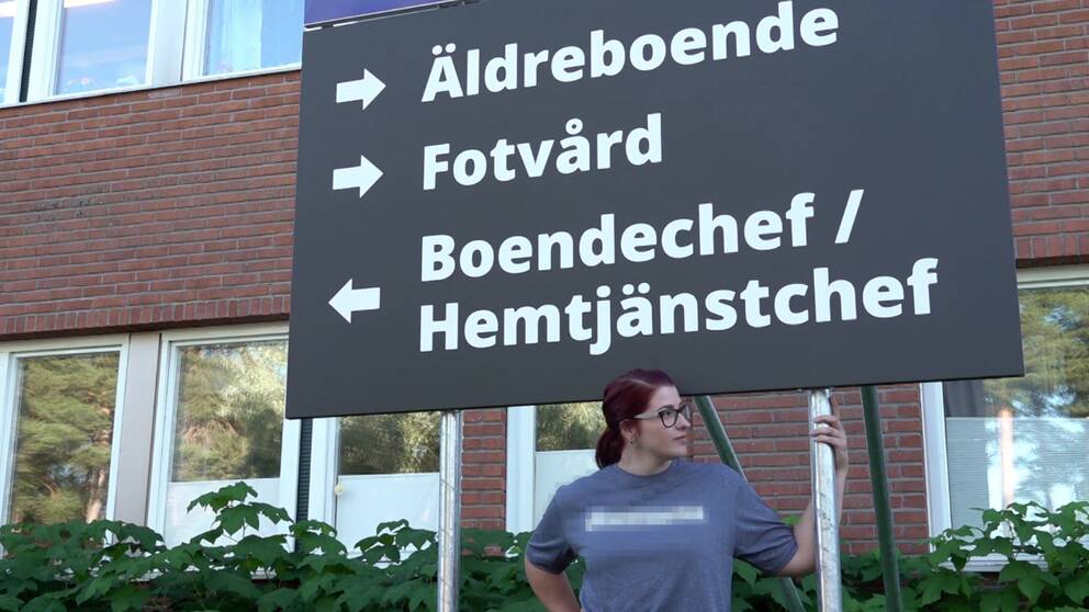 kvinna står under stor skylt med pilar till äldreboende, fotvård och boendechef/hemtjänstchef