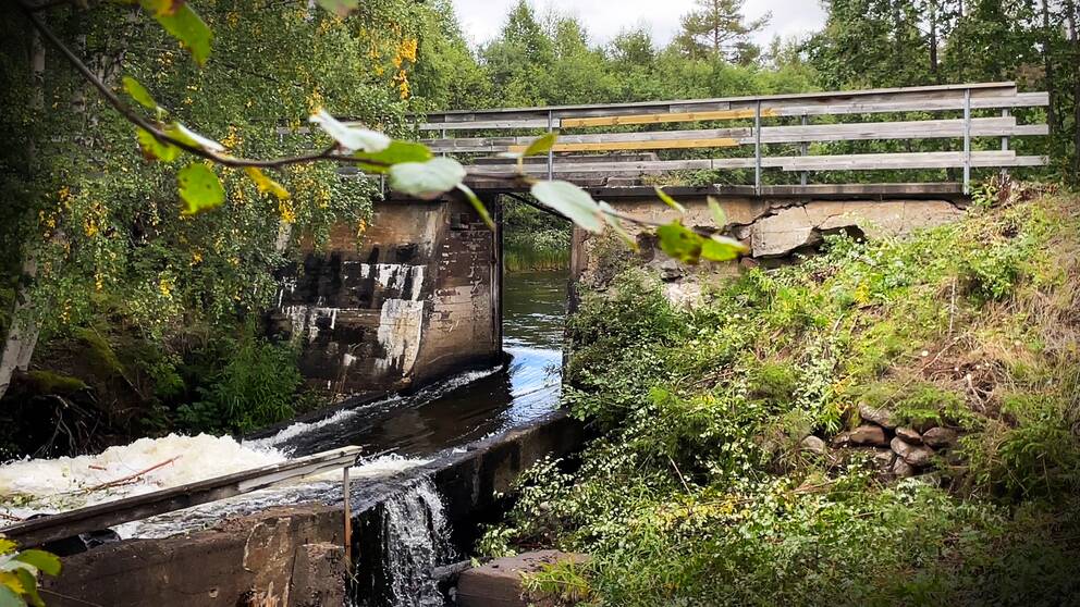 En bild på en sliten kraftverksdam, man kan skymta en slags bro som går över ett vattendrag.