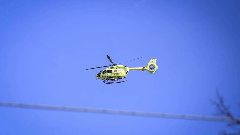 En ambulanshelikopter flyger under blå himmel.