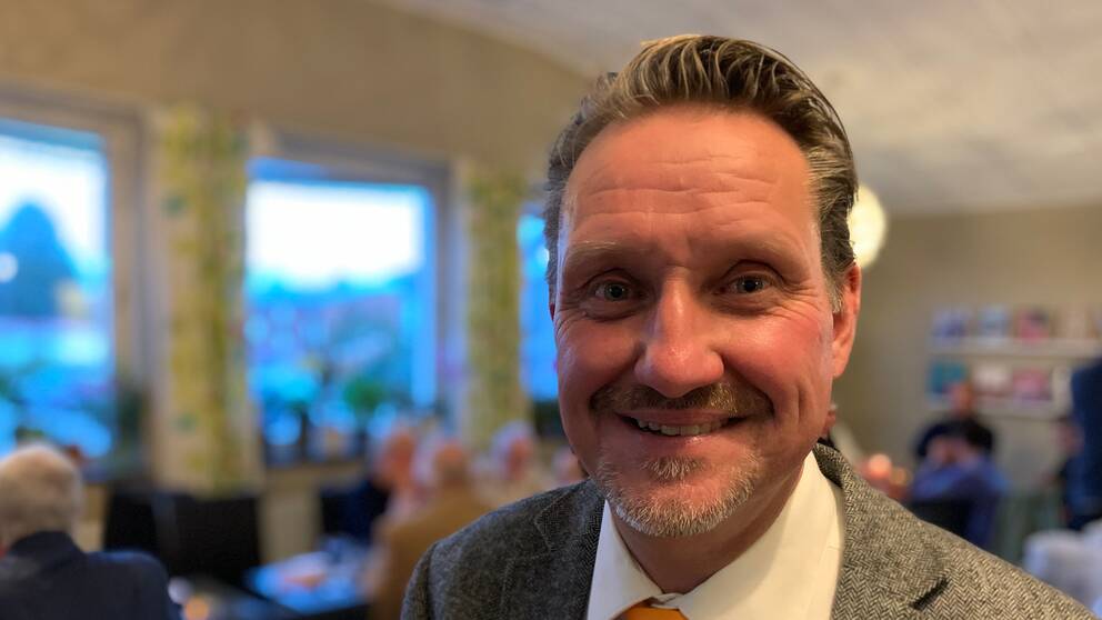 En man med kort grått hår och kort skägg och grå kostym.
