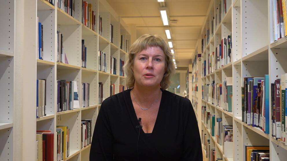 en medelålderskvinna står mellan bokhyllorna i ett bibliotek