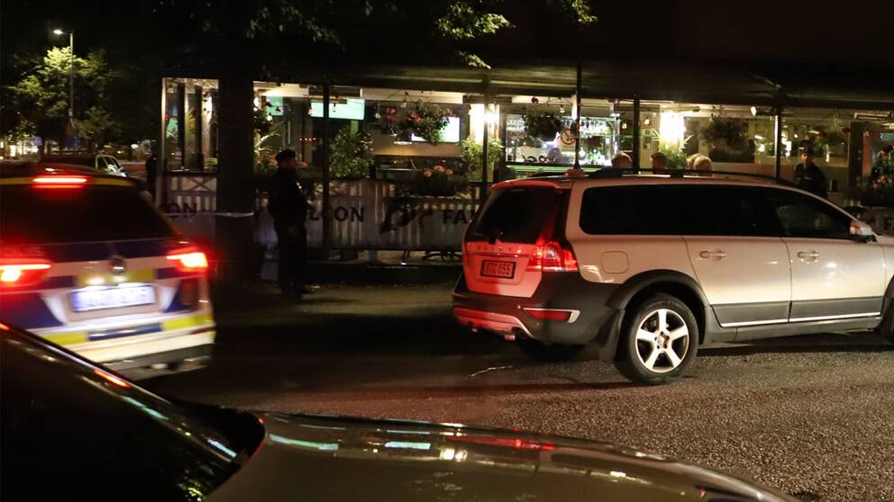 En polisbil och en annan bil står parkerade på vägen utanför en upplyst restaurang.