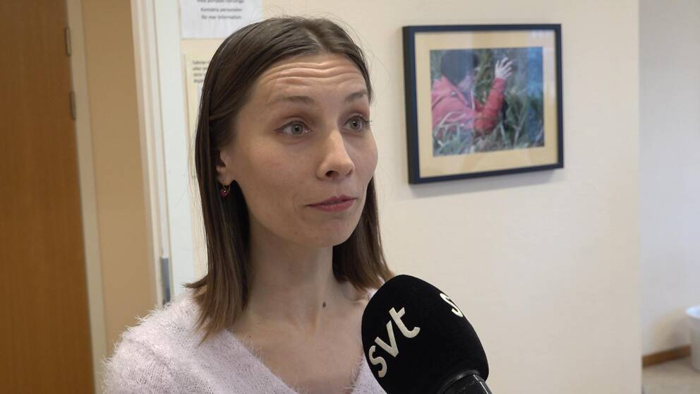 ung smal kvinna, brunt halvlångt hår, vit tröja, intervjuas av SVT, i ett rum, en tavla på väggen, vita väggar.