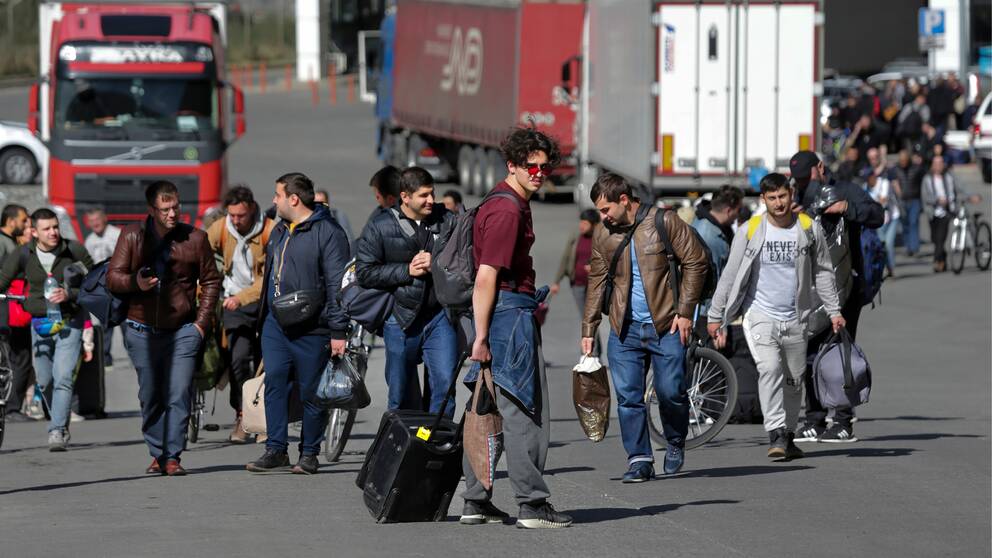 Män går på rad med resväskor efter att ha flytt från Ryssland.