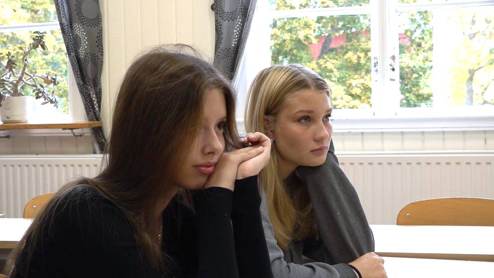 Halvbild på Amelie Engström, brunt långt hår, och Moa Florenius, blont långt hår, sitter i skolbänken och tittar framåt.