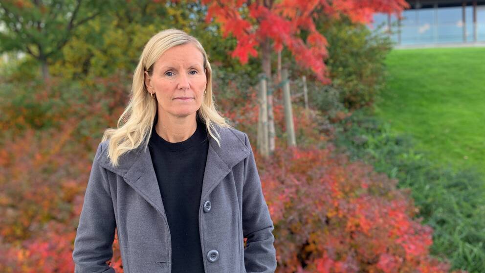 Linda Larsson, enhetschef på individ- och familjeomsorgen i Skellefteå kommun ,står utomhus. i bakgrunden syns träd i olika höstfärger. Hon är blond och klädd i en svart tröja och grå kappa.