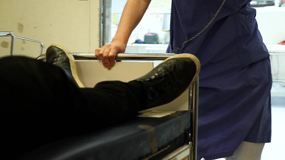 Närbild på ben på en patient som skjutsas i en sjukhussäng av personal i ett sjukhus.