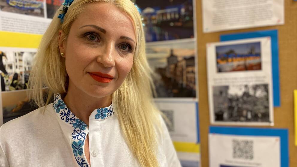 Viktoriya Lunova står framför en vägg med bilder från Ukraina.