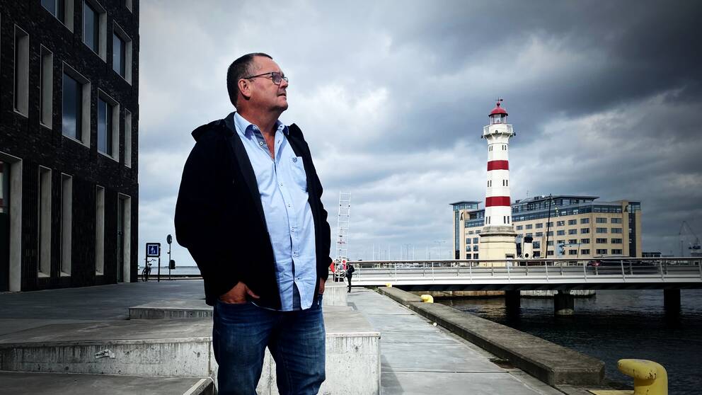 En bild på en man i skjorta och svart jacka som tittar ut över en hamn i Malmö, där intervjun sker.