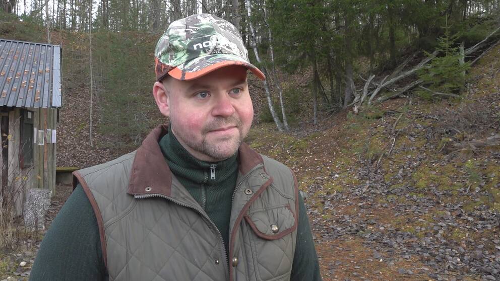 Landsbygdsminister Peter Kullgren står i skogen och har på sig gröna jaktkläder och en keps med kamouflagemönster.