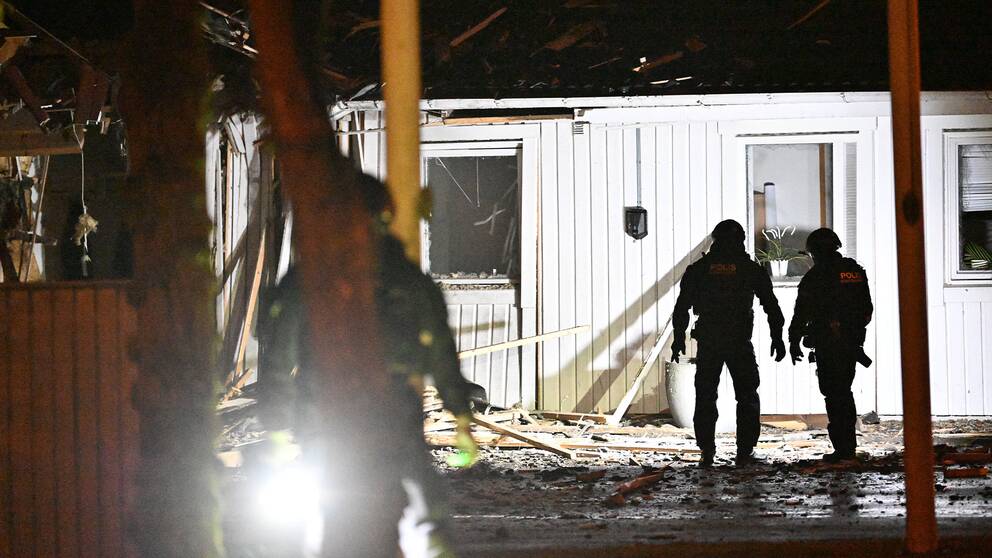 Bombtekniker på plats vid en vit byggnad efter en explosion.