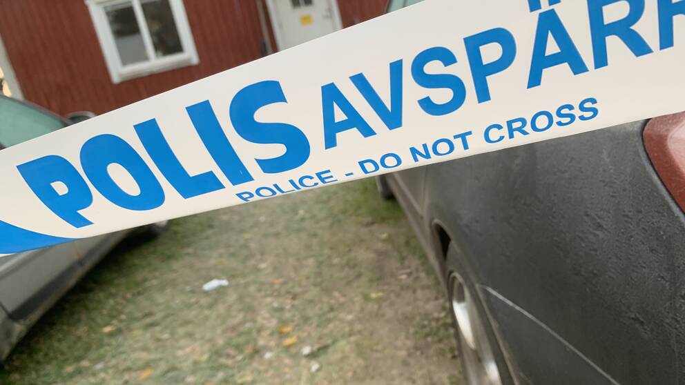Ett polisavspärrningsband, i bakgrunden syns ett rött hus.