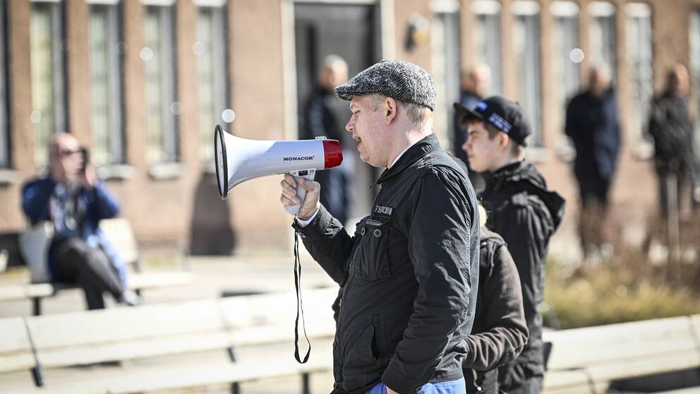Man med keps håller tal till en folksamling.