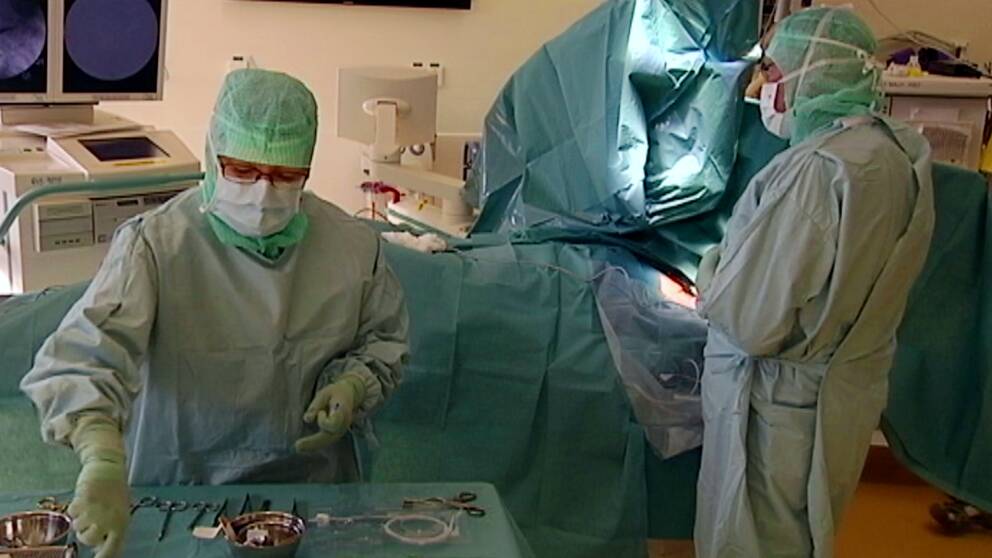 Genrebild på pågående operation i kirurgisal där sjukvårdspersonal arbetar iklädda skyddskläder och munskydd.