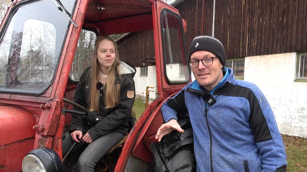 Eliška Valečková sitter i en röd gammeldags traktor som paret köpt in för att hålla kostnaderna nere. Thomas Eliasson står lutad mot ett av de stora däcken.