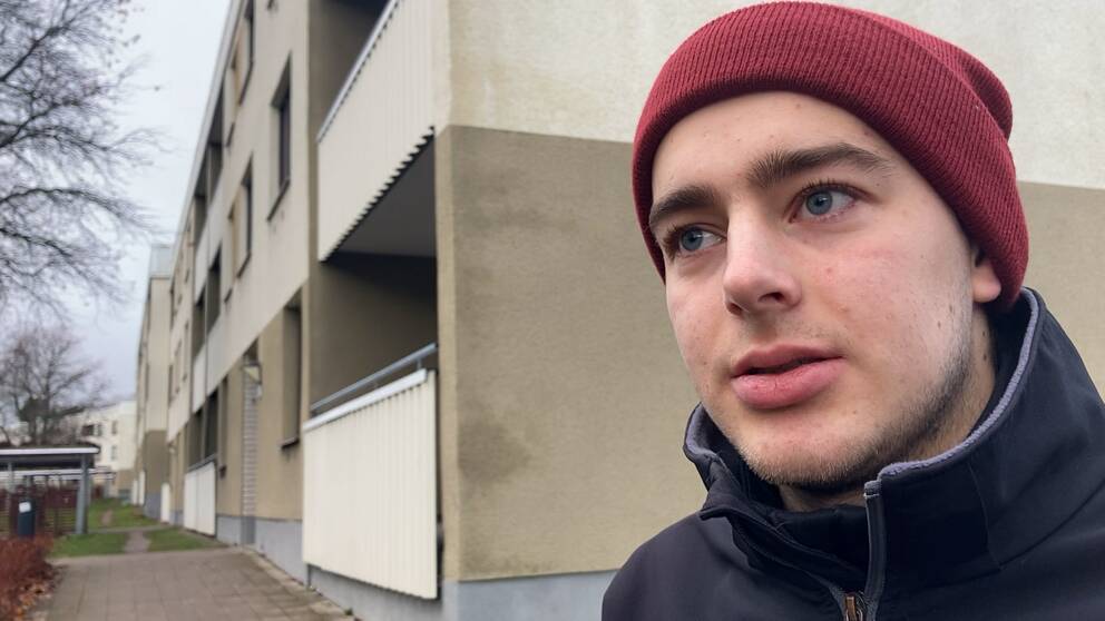 Bild på Johannes Andersen, student som bor vid platsen där dödsskjutningen inträffade på campus i Sätra på lördagskvällen. Han har på sig en röd mössa och står framför ett bostadshus.