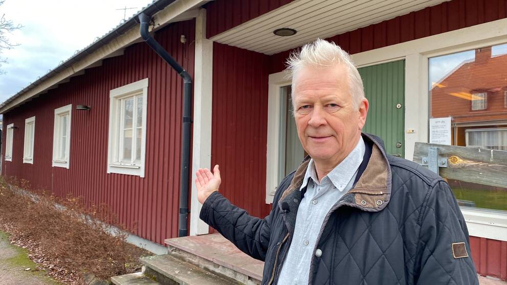 en vithårig man som är kommundirektör i Mora kommun, pekar mot ett hus som kommunen ska dra ner värmen i – så att de spar pengar.