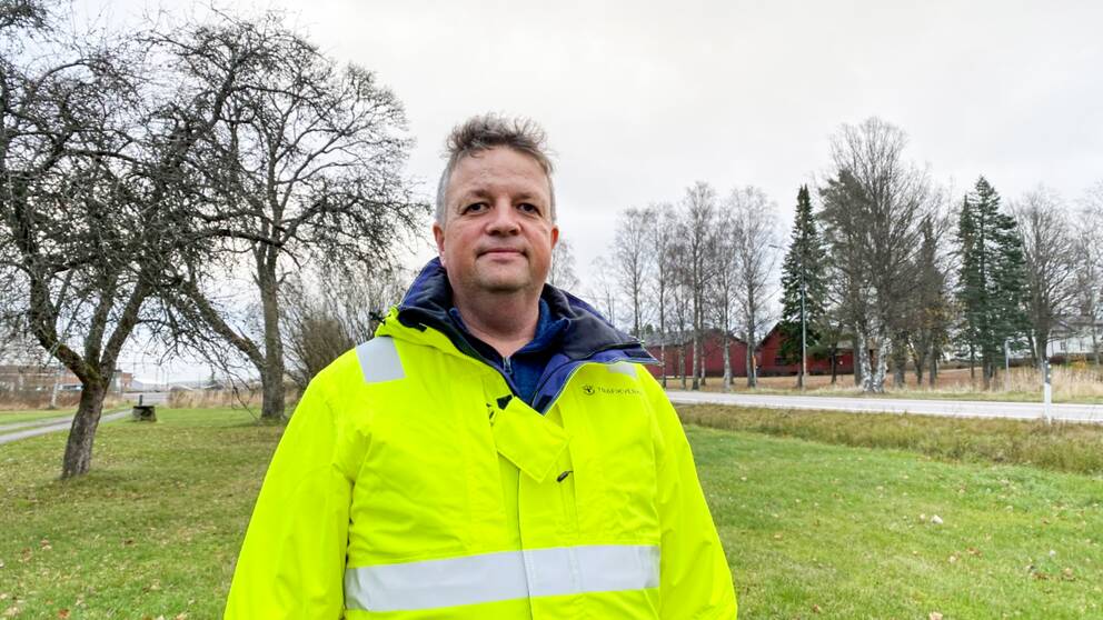 En man med reflexjacka står på gräset bredvid en väg.