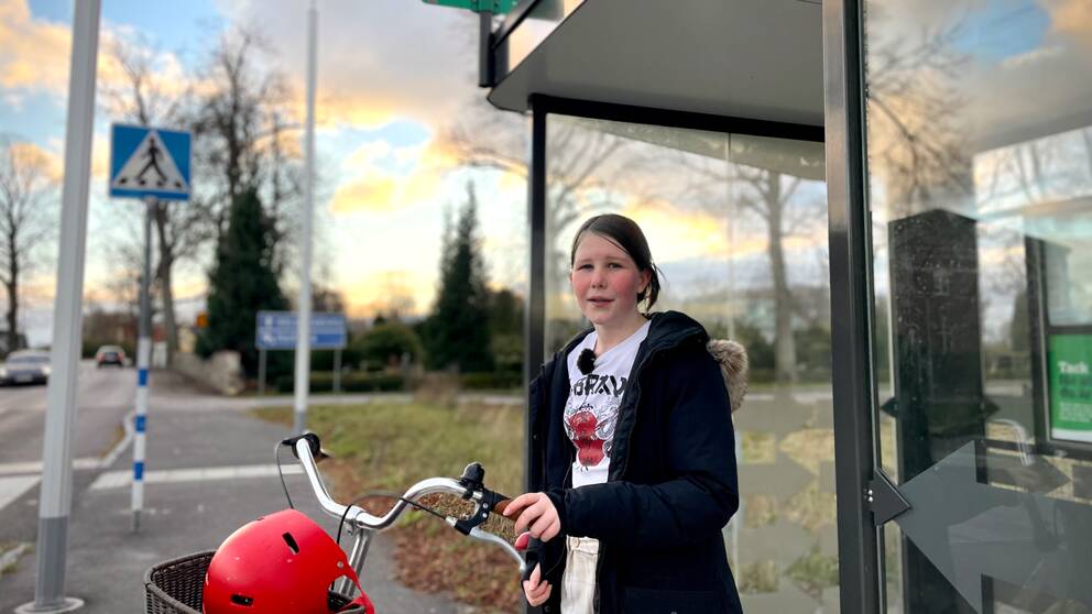 Flicka står vid sin cykel vid en busskur i Allerum