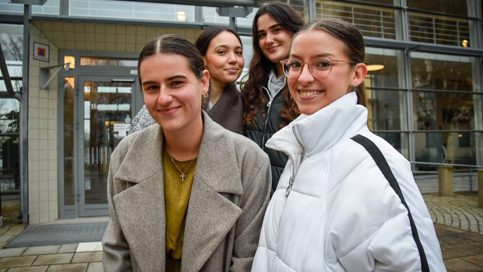 Fyra unga utlandsstudenter poserar fram Högskolan Gävles huvudingång i glas.