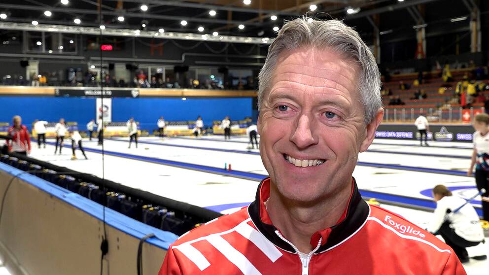 Peja Lindholm ler brett. Ishall i bakgrunden där Curling-EM i Östersund avgörs.