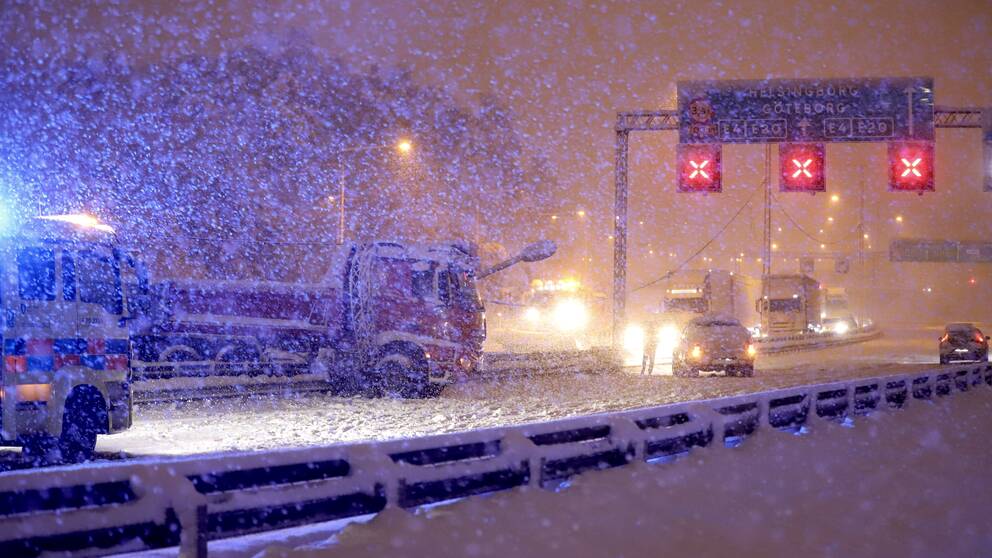 Bilar står i kö medan ett kraftigt snöfall skapar ett tjockt snötäcke.