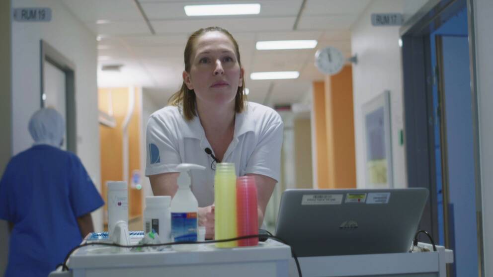 en sjuksköterska står och hänger på ett bord i en korridor på Falu lasarett.