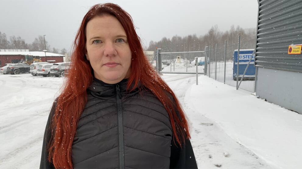 En kvinna med rött långt hår, har en svart täckjacka, står utomhus i snöväder. Hon heter Helena Andersson, ordförande för Postklubben i Dalarna.