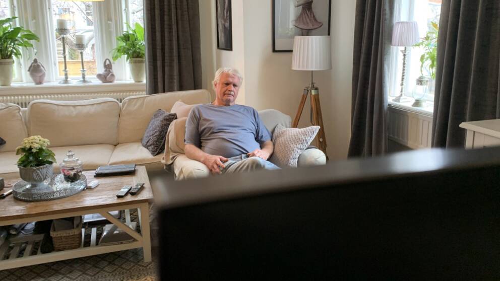 En äldre man sitter i en fåtölj och ser på tv. 
