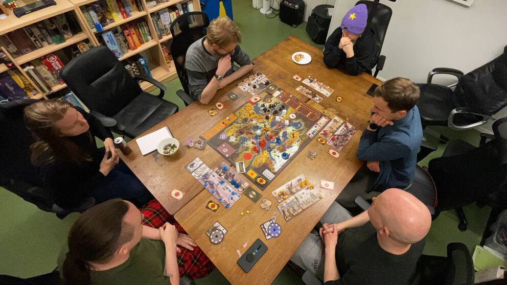 Sex personer sitter samlade runt ett träbord med ett brädspel på. Personerna är med i Karlstad spelkulturförening som nu är nominerade till att bli årets förening inom Sverok.