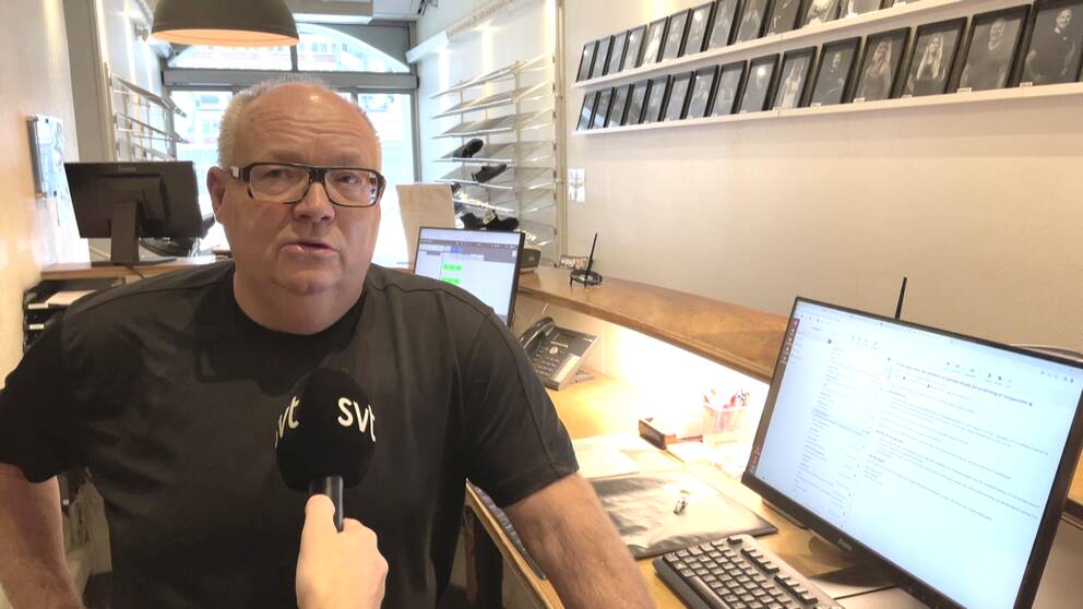 Man med svart T-shirt och glasögon står bredvid en dator.