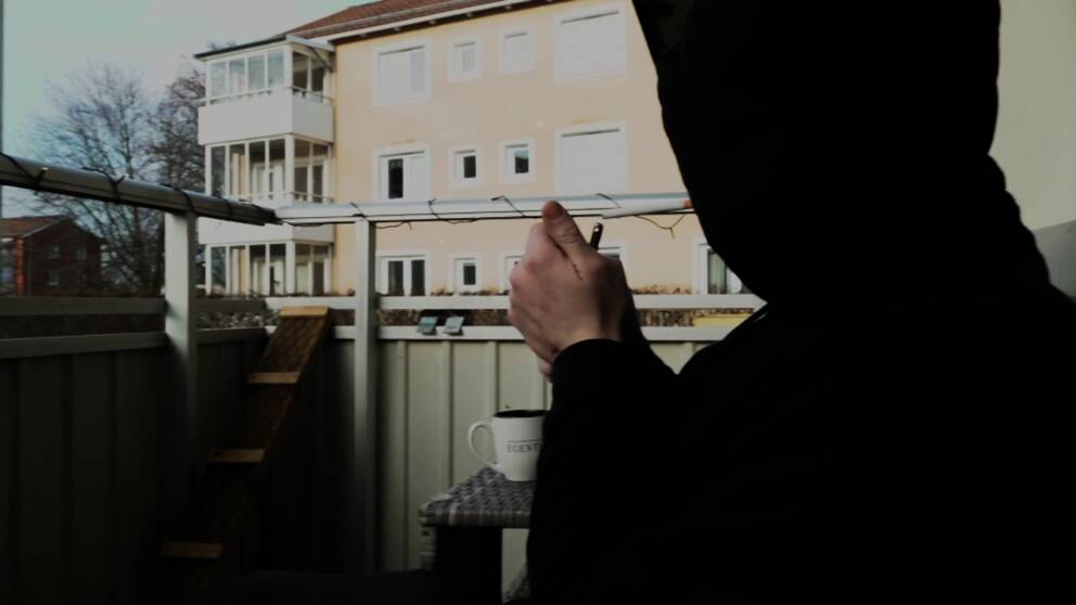 En man i luvtröja sitter på en balkong och tänker en cigarett