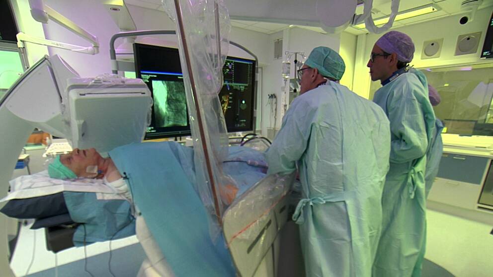 En kvinna ligger på ett operationsbord, tre vårdpersonal står över henne och kollar på en skärm