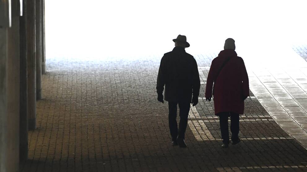 Två pensionärer på promenad vid Tegelbacken i Stockholm. Gubben till vänster bär hatt.