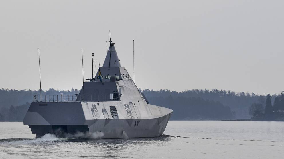 Grå pansarbåt åker i vattnet i skärgården.