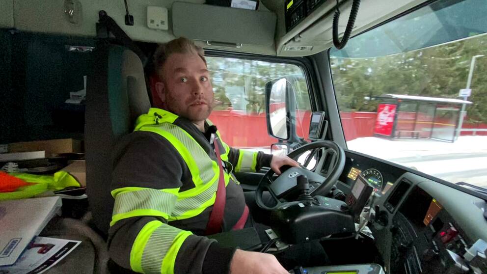 Henrik Danielsson iklädda reflexgula kläder, sitter i förarhytten på en lastbil i Luleå.