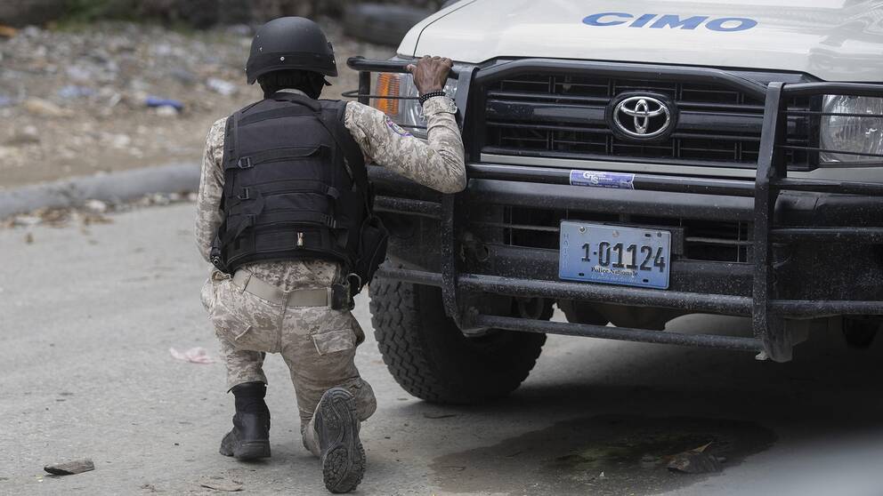 En polis tar skydd bakom en bil under en anti-gängoperation i Croix-des-Missions norr om Port-au-Prince, Haiti. Arkivbild.