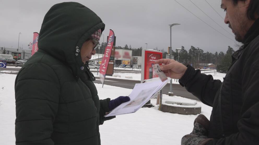 Kvinna med luva håller ett papper i handen i vintervitt landskap