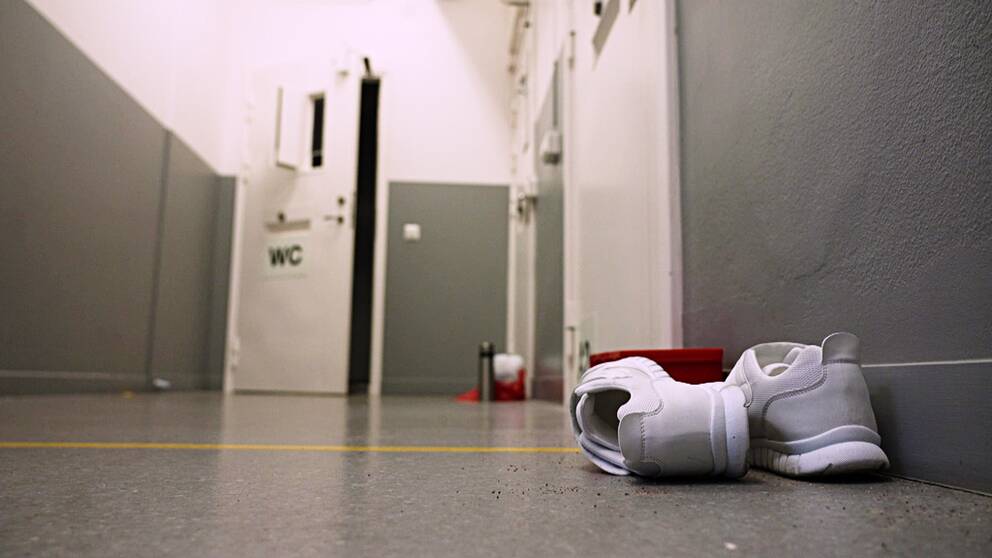 Ett par skor står i förgrunden utanför en toalett inne på en anstalt.