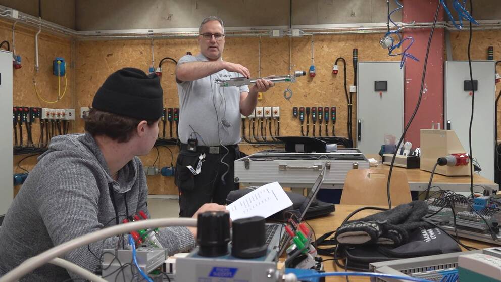 Joakim Fogelberg, som är lärare på El- och energiprogrammet på Bäckadalsgymnasiet i Jönköping, står framför en elev och undervisar inne i en verkstad på gymnasiet.