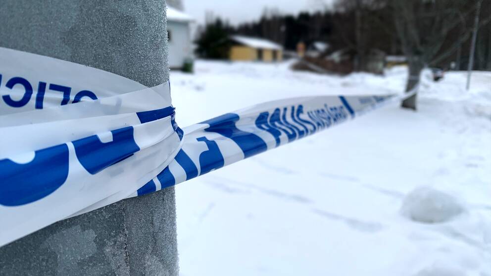 Bild på polisens avspärrningsband som sitter runt en lyckstolpe och ett träd på andra sidan. Marken är snötäckt.