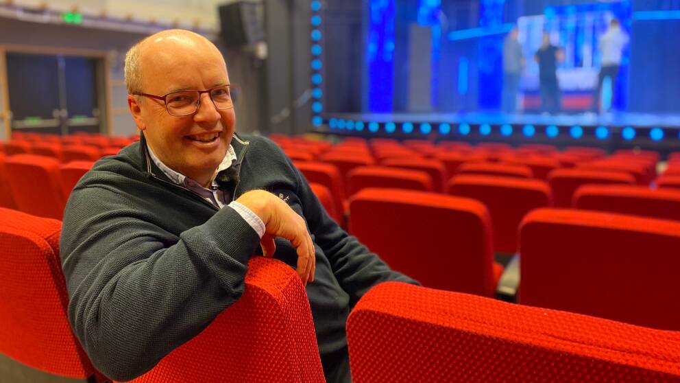 Bild på en man med glasögon som sitter i en röd teaterstol i en salong. Mannen heter Magnus Wernersson och är oroducent på Falkenbergsrevyn. I klippet får vi se bilder från den nya revyn.