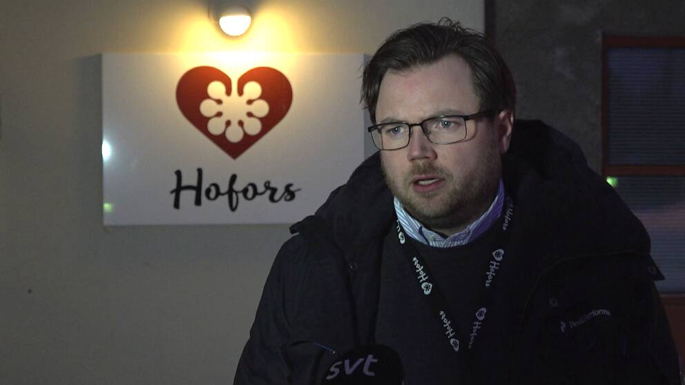 Man i glasögon och skägg framför en upplyst skylt där det står Hofors.