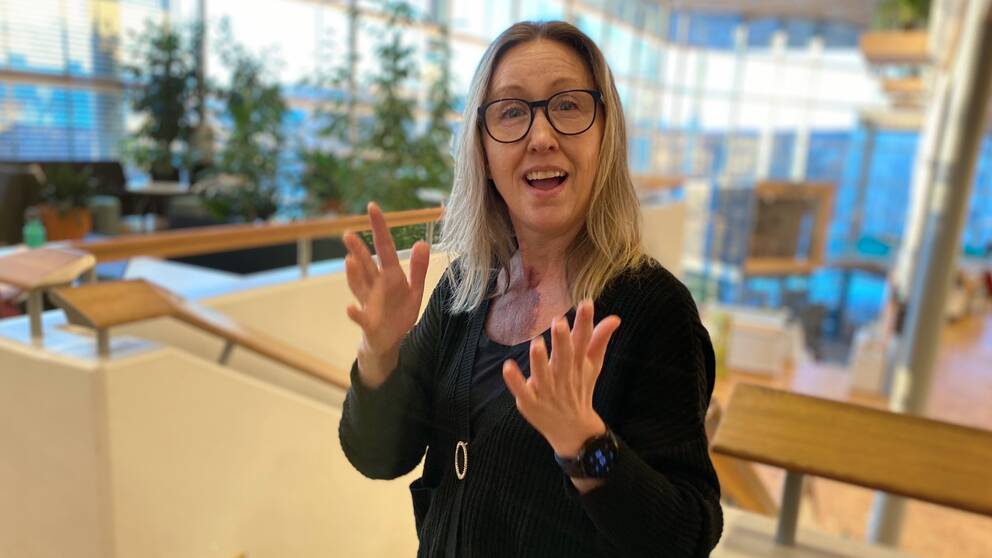 Anna Sofia Såthe – en medelålders kvinna med glasögon – gör teckenspråkets tecken för leva.