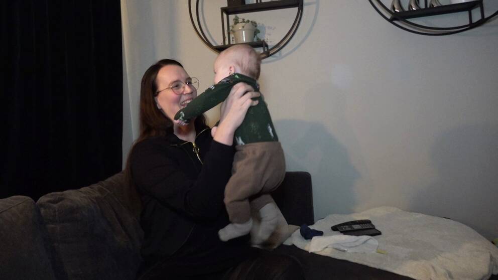Hanna Nordahl från Örnsköldsvik, som blev igångsatt sitter hemma i sitt vardagsrum och håller upp sin bebis och tittar den i ögonen medan hon ser glad ut.