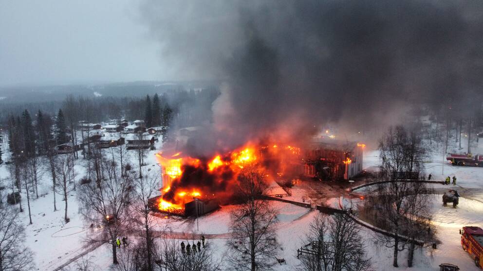 En stor träbyggnad står i brand.